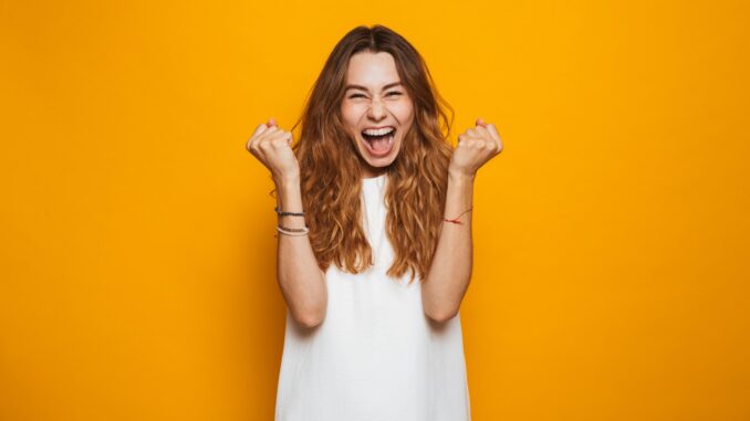 Portrait of a happy young girl screaming celebrating isolated over yellow background. old crap