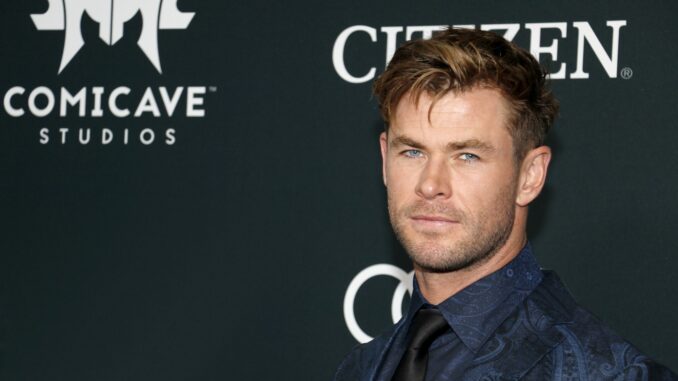 Chris Hemsworth in a black suit and shirt, showing no sign of having been inflated