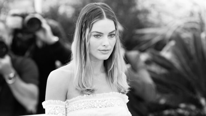 Margot Robbie wearing a white strapless top. Black and white. Not looking as hot as if she wore a sweater.