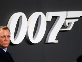 Daniel Craig in a suit in front of a 007 poster for the release fo No time to die