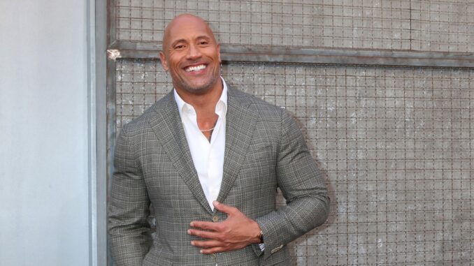 Dwayne Johnson in a grey jacket leaning against a wall. Vin Diesel and The Rock