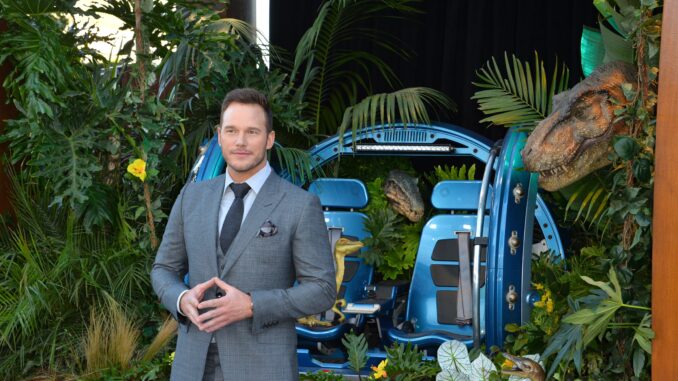 Chris Pratt voice standing in front of a set from Jurassic world