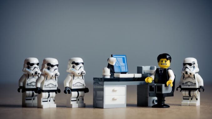 SEveral Lego stormtroopers surround a legoman at a desk. New Lego Star Wars Game