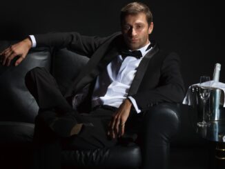 A billionaire playboy in a tux lounging on sofa with champagne