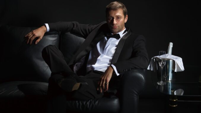 A billionaire playboy in a tux lounging on sofa with champagne