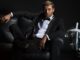 A billionaire playboy in a tux lounging on sofa with champagne