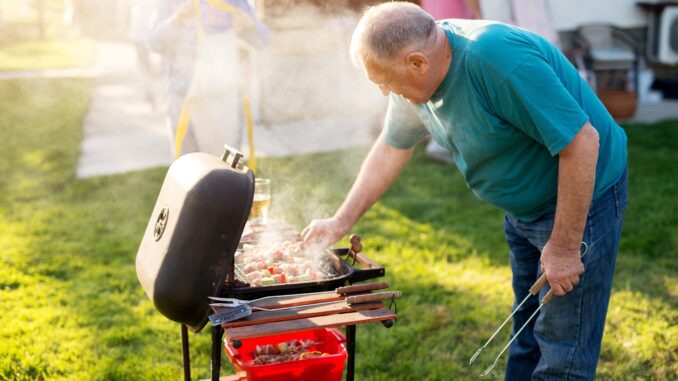Elderly man is rotating meat and vegetable on a stick that is being grilled on the vintage grill. ferris bueller spin-off