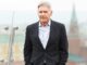 Harrison Ford, wearing a dark suit with white shirt and no tie