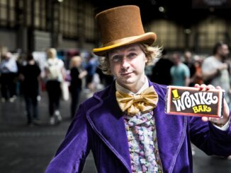 male cosplayer dressed as young Willy Wonka from the Charlie and the Chocolate factory books holding a Wonka bar of chocolate.
